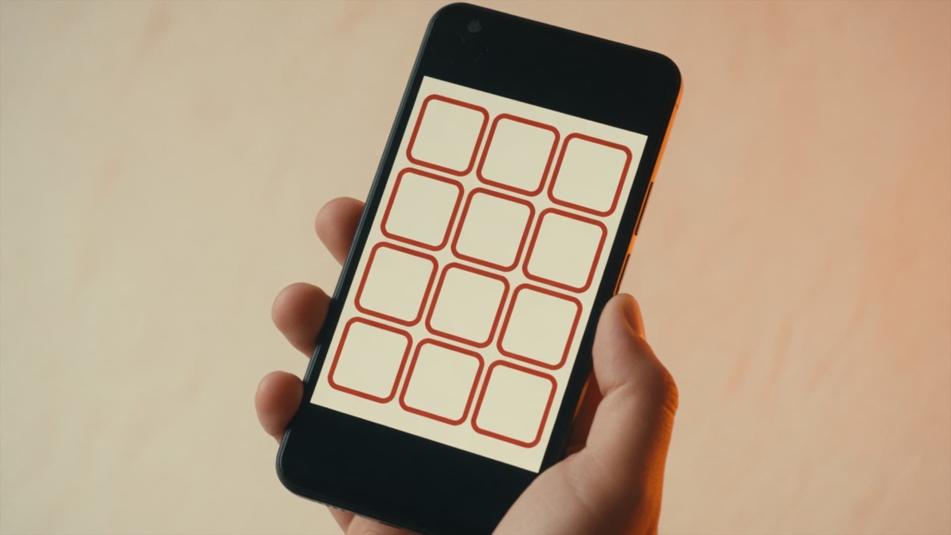 A hand holding a phone with a simple cream and red app on the screen