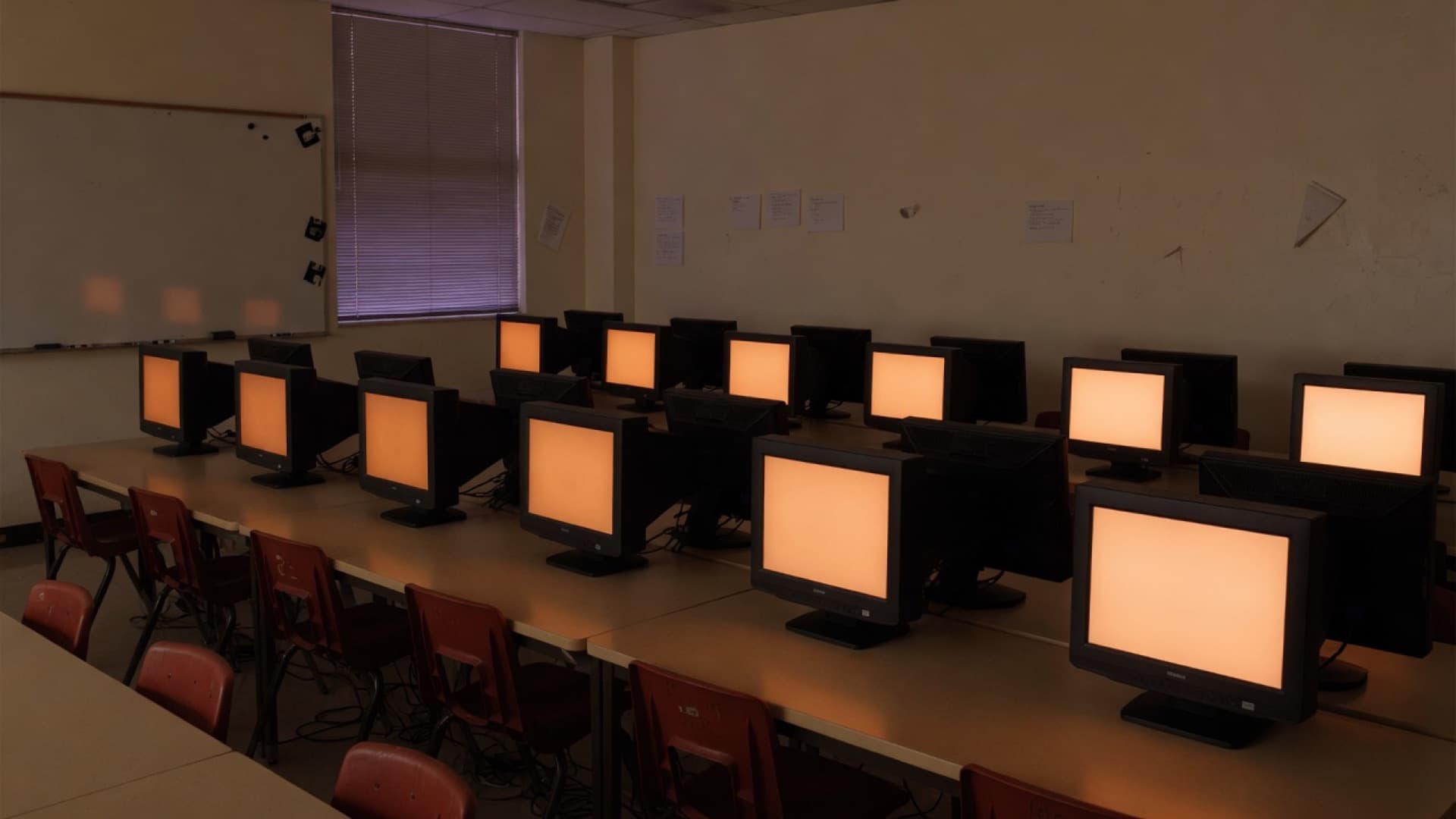 A darkened computer lab with monitors glowing warm orange